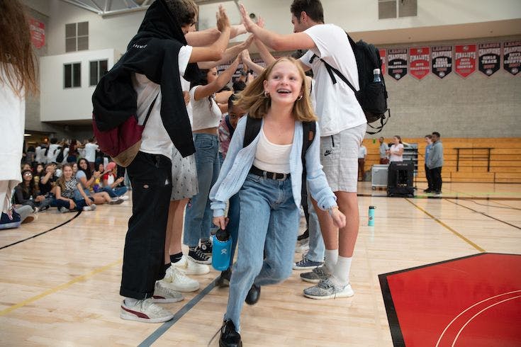 Child running through a high-five tunnel formed by teens in a gym