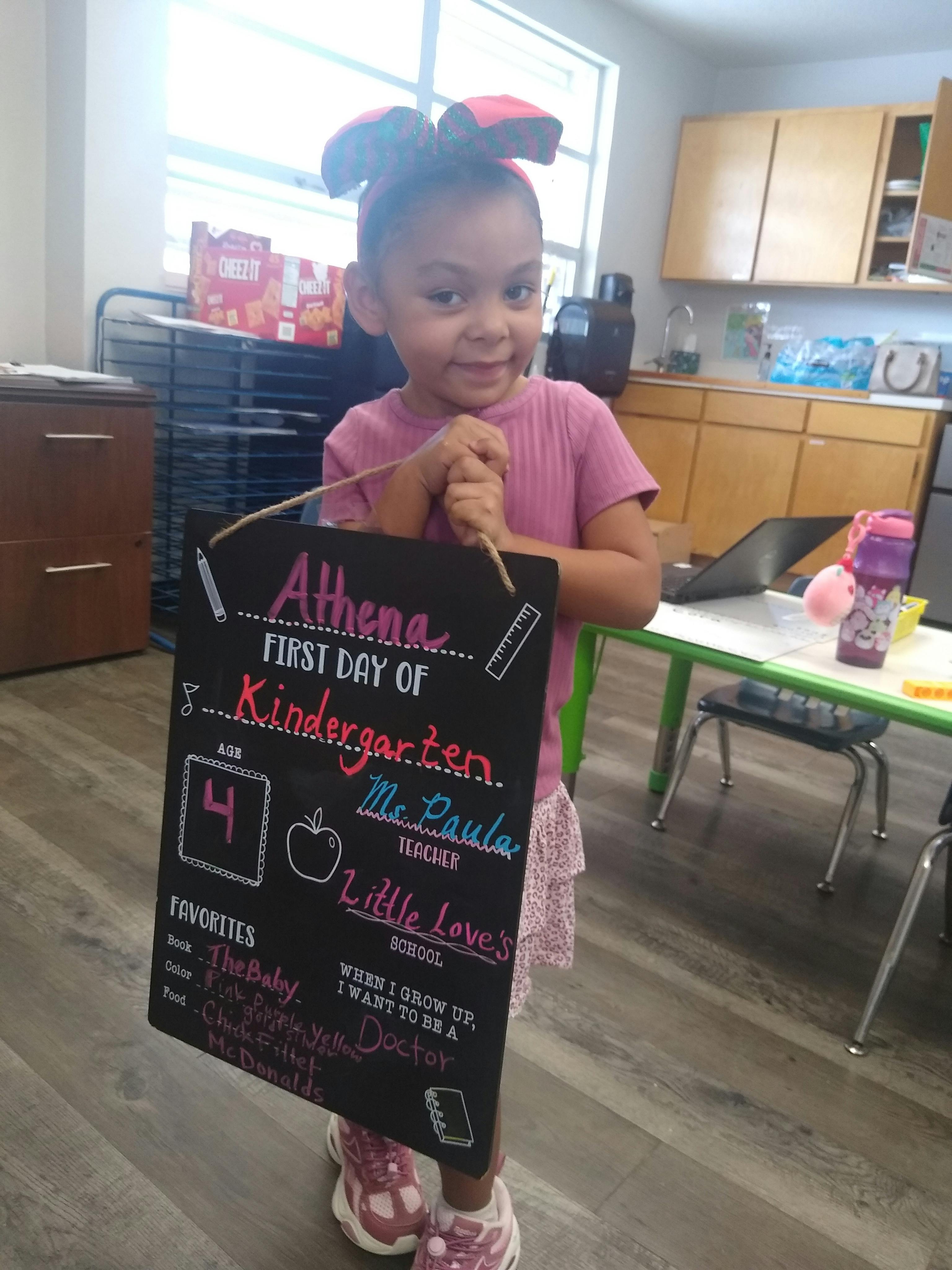 Child holding a first day of kindergarten sign in a classroom