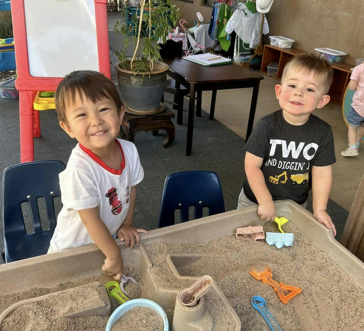 Two smiling children playing in a sandbox with toys