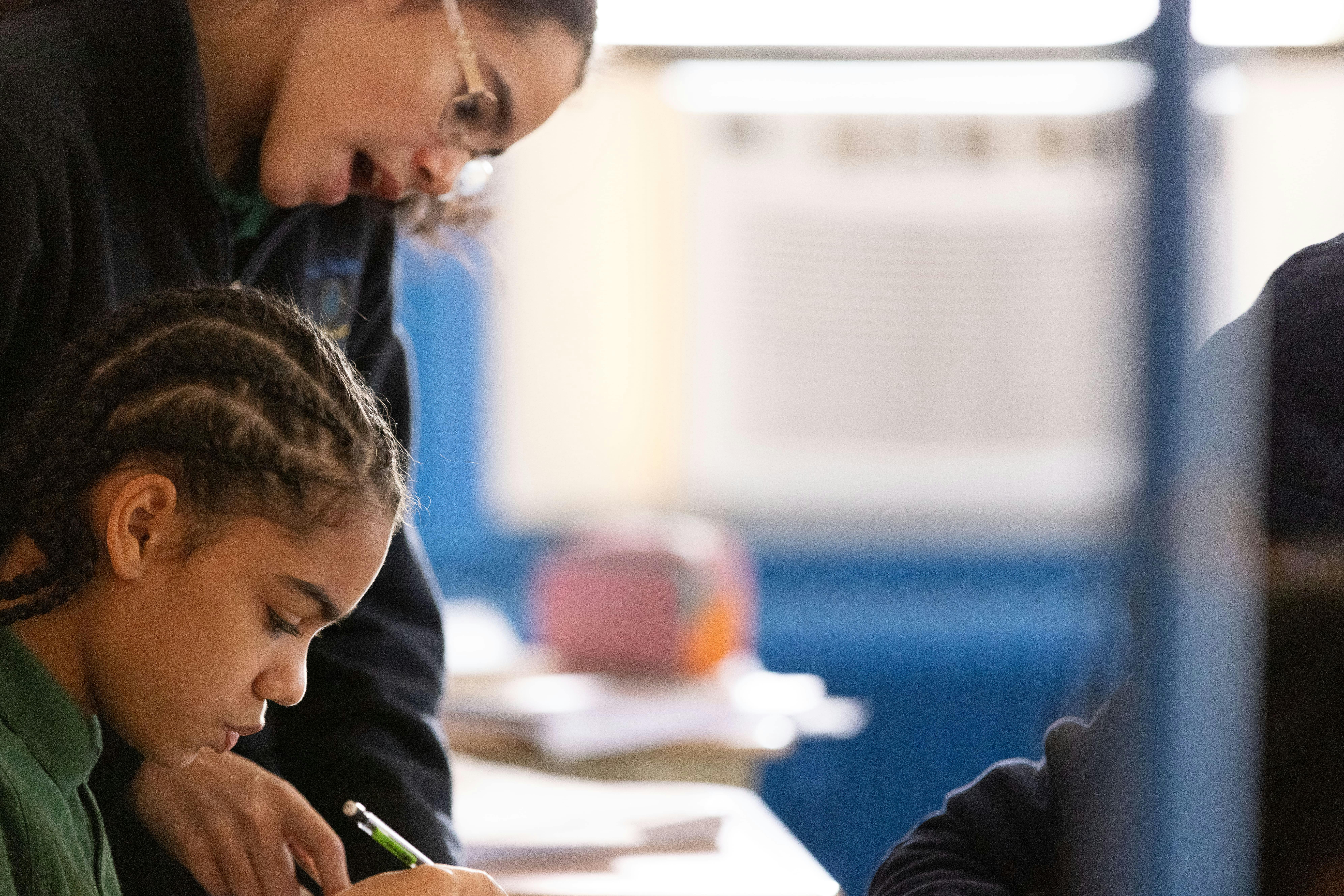 Adult person helping a child write in a classroom