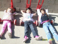 Three children lying on the ground next to red scooters