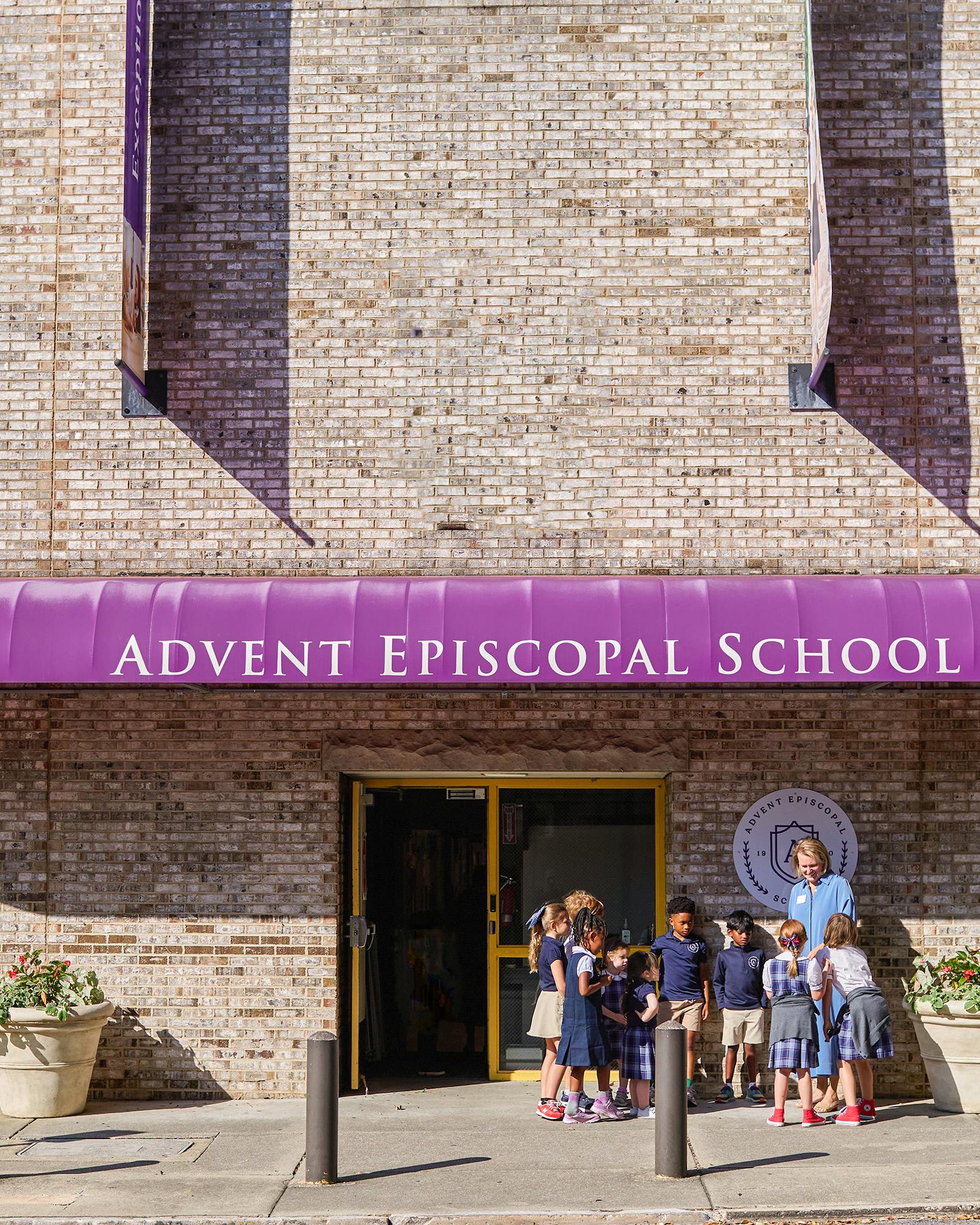 Group of children standing outside a school entrance with a woman