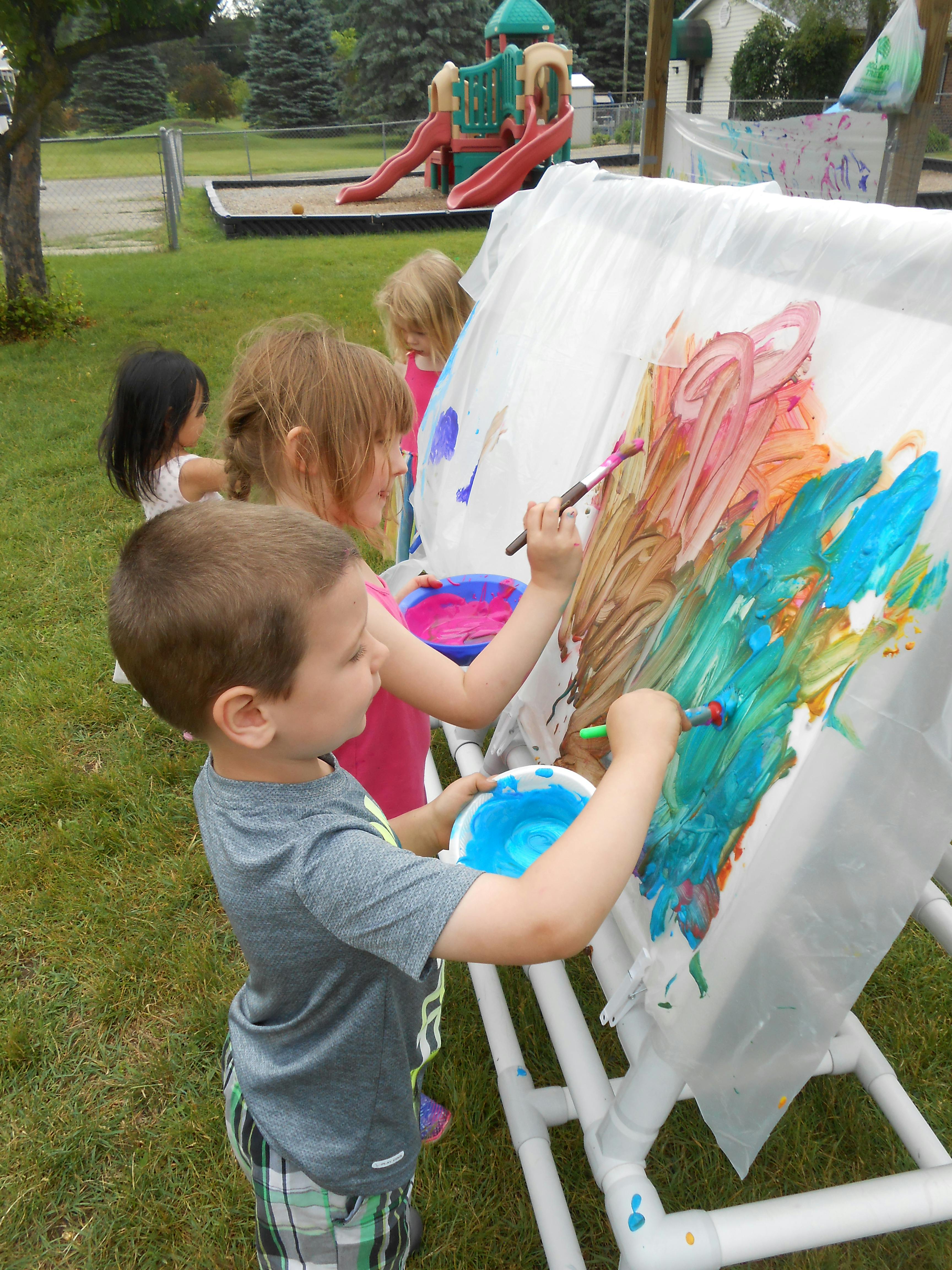 Children painting on an easel outdoors