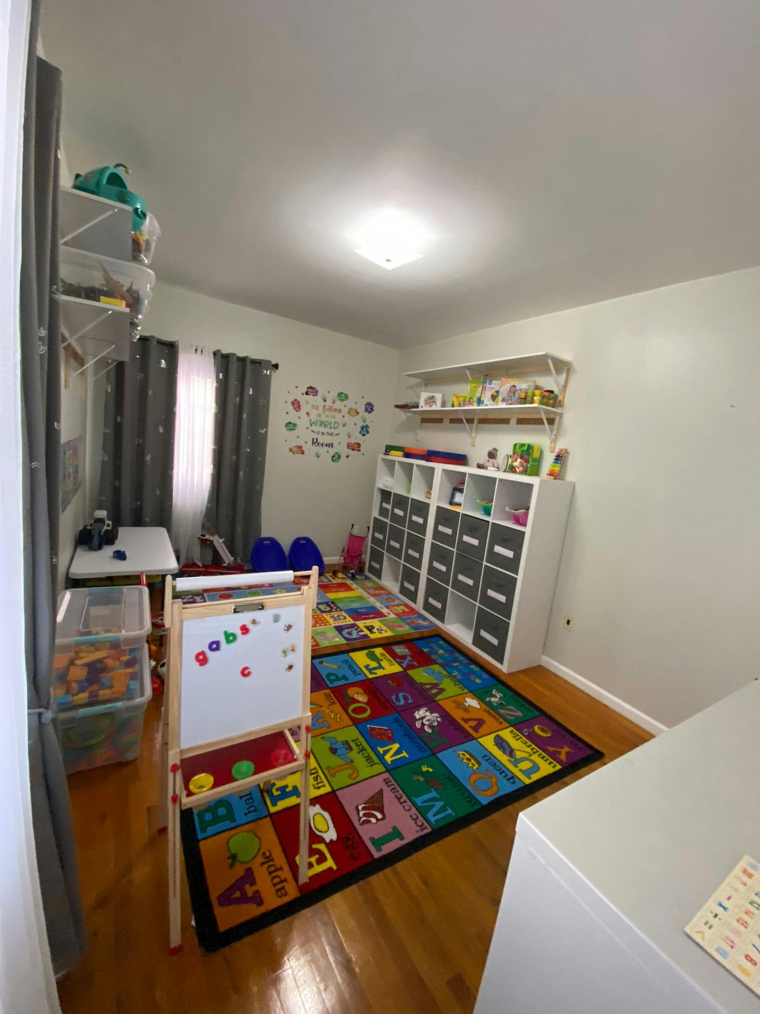 Playroom with an alphabet rug, whiteboard easel, and storage shelves