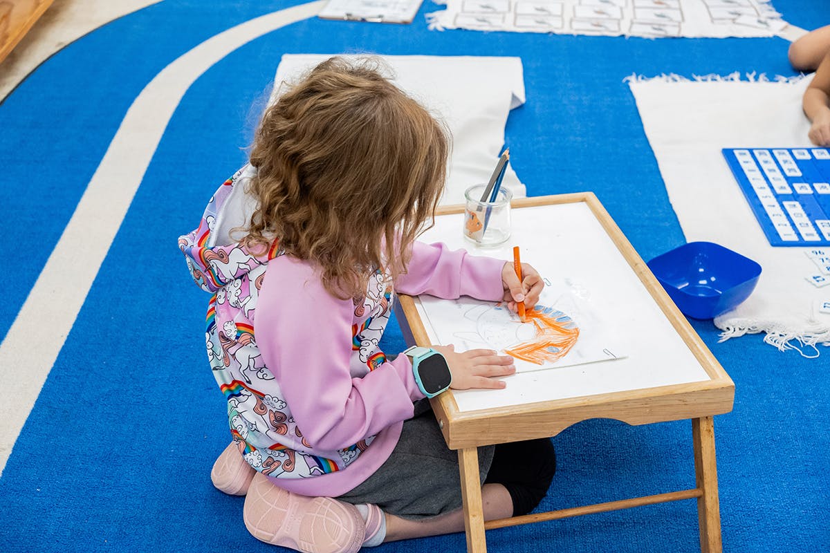 Child drawing on paper at a small table on the floor