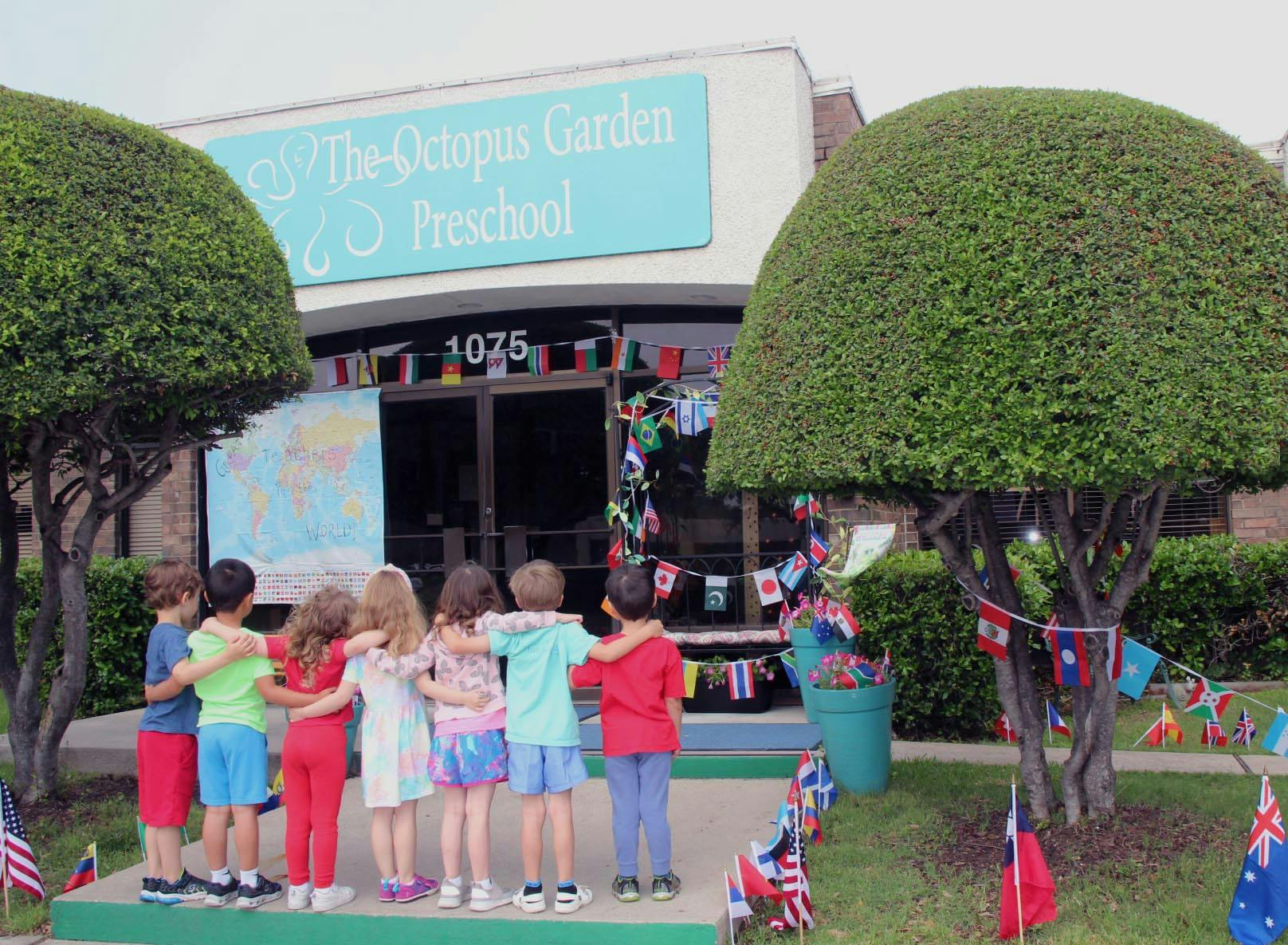 Children standing with arms around each other in front of a preschool