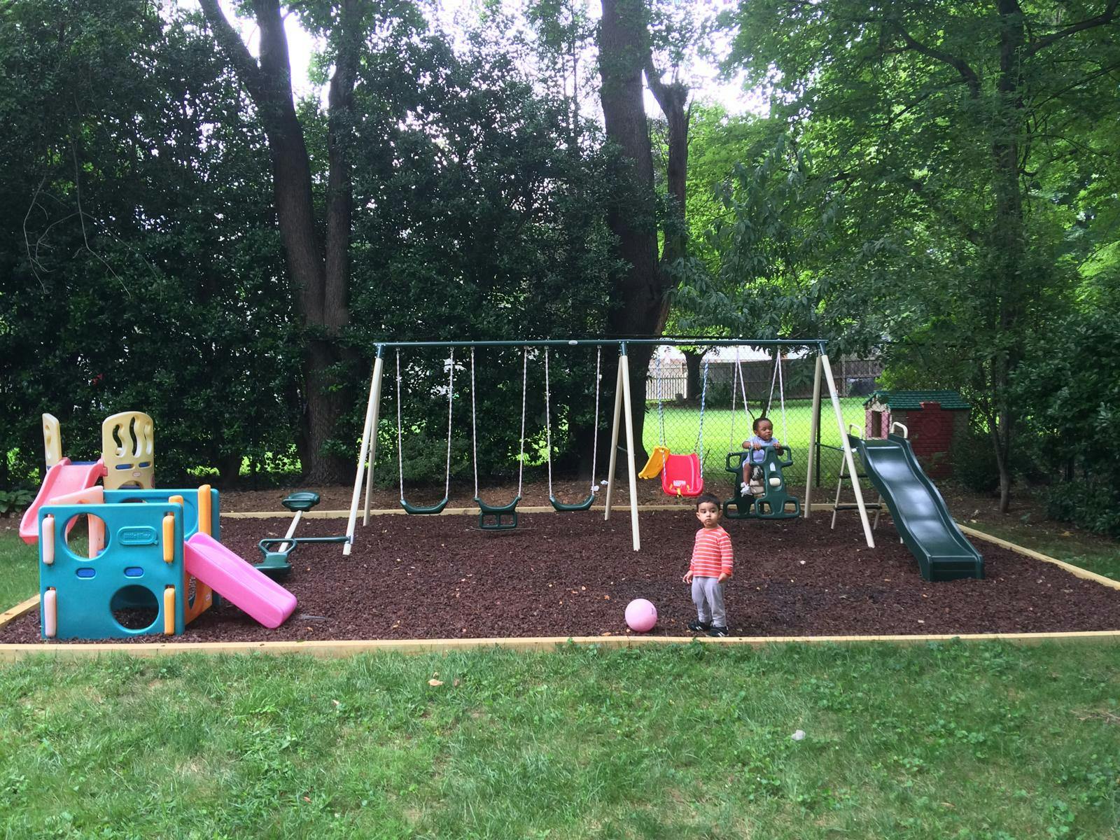 Two children on a playground with swings, slides, and a ball