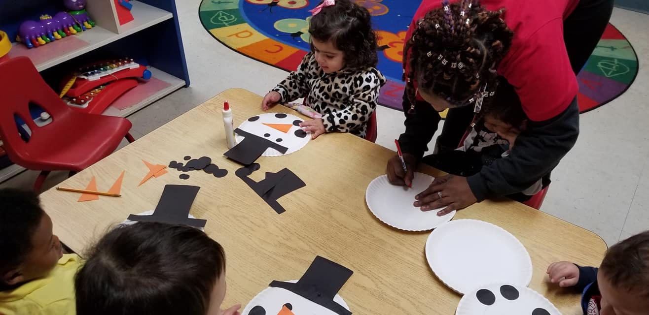 Adult and child making snowman crafts at a table in a classroom
