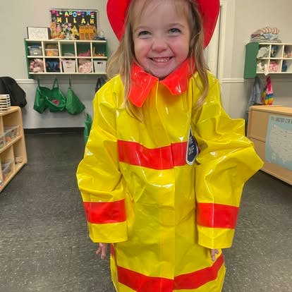 Child wearing a yellow firefighter costume and red helmet in a classroom