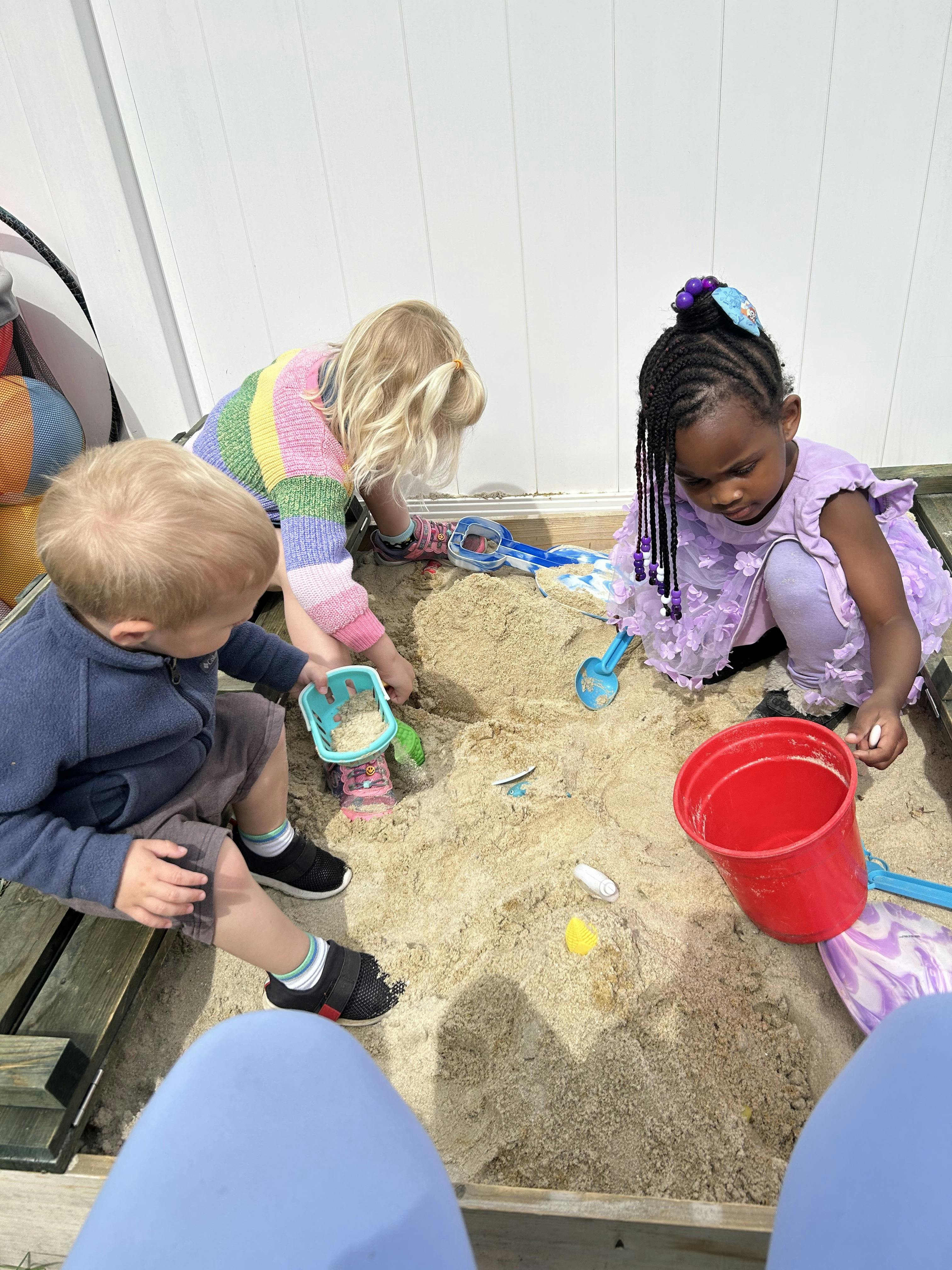 Three children playing together in a sandbox with various toys