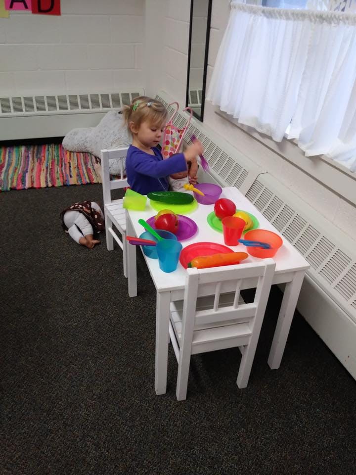 Child playing with colorful toy dishes at a small white table