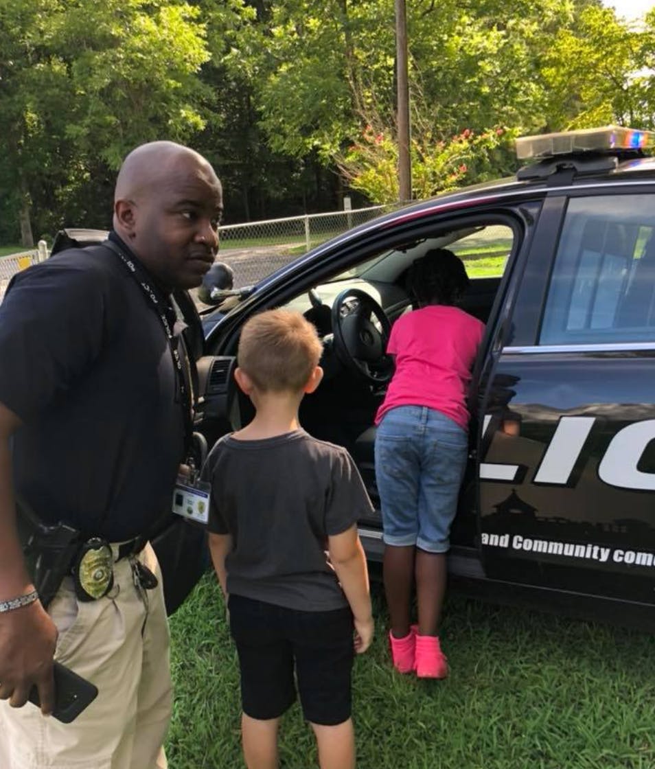Person in uniform with two children looking into a police car