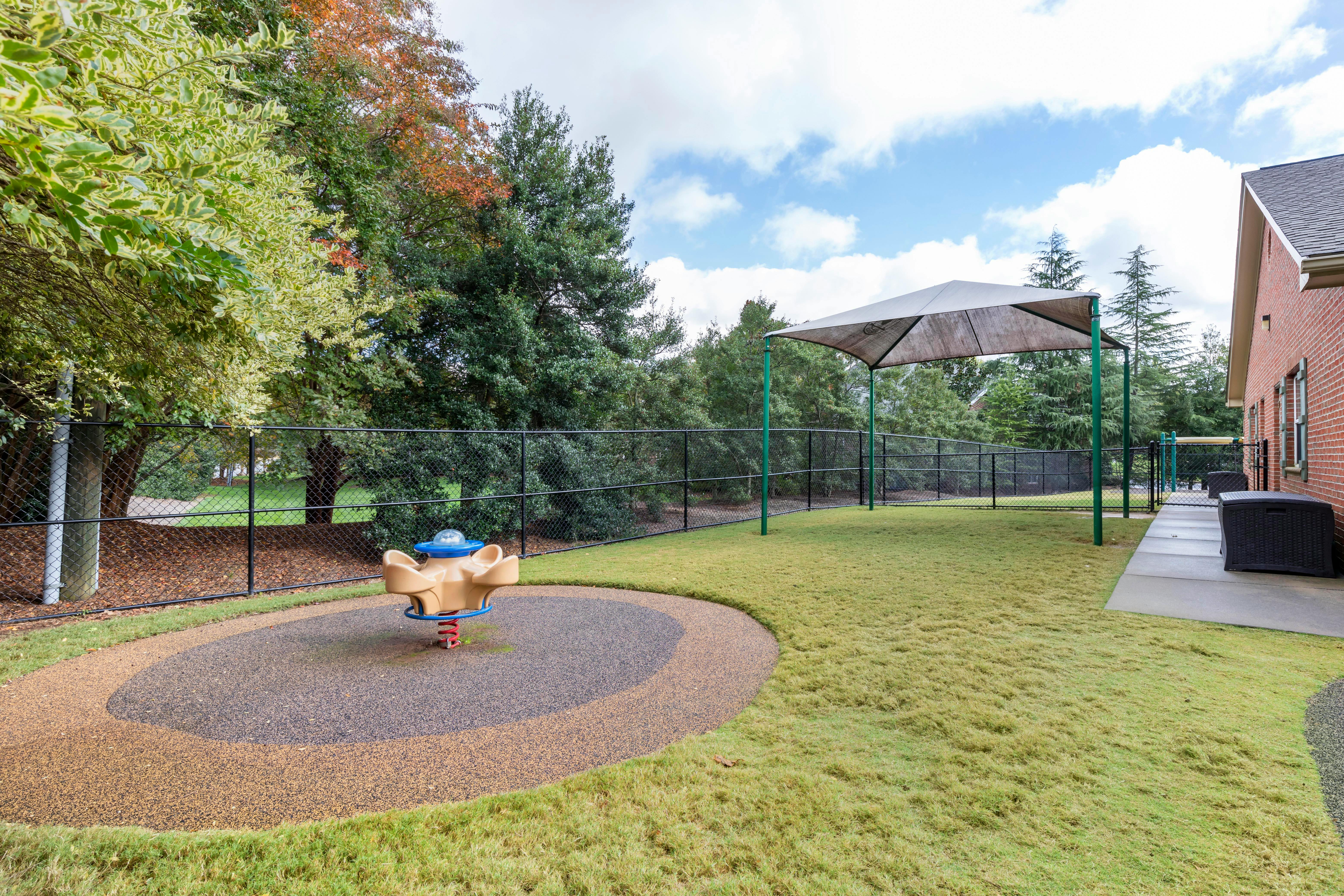 Playground area with a spring rider, shade canopy, grass, and fence