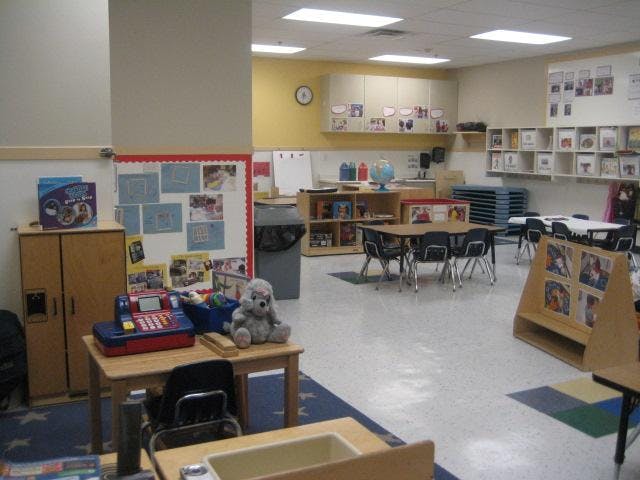 Empty classroom with small tables and chairs, shelves, and a play cash register