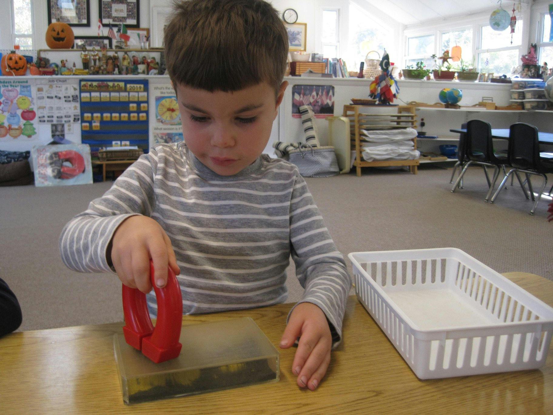 Child using a red magnet on a clear block at a table in a classroom