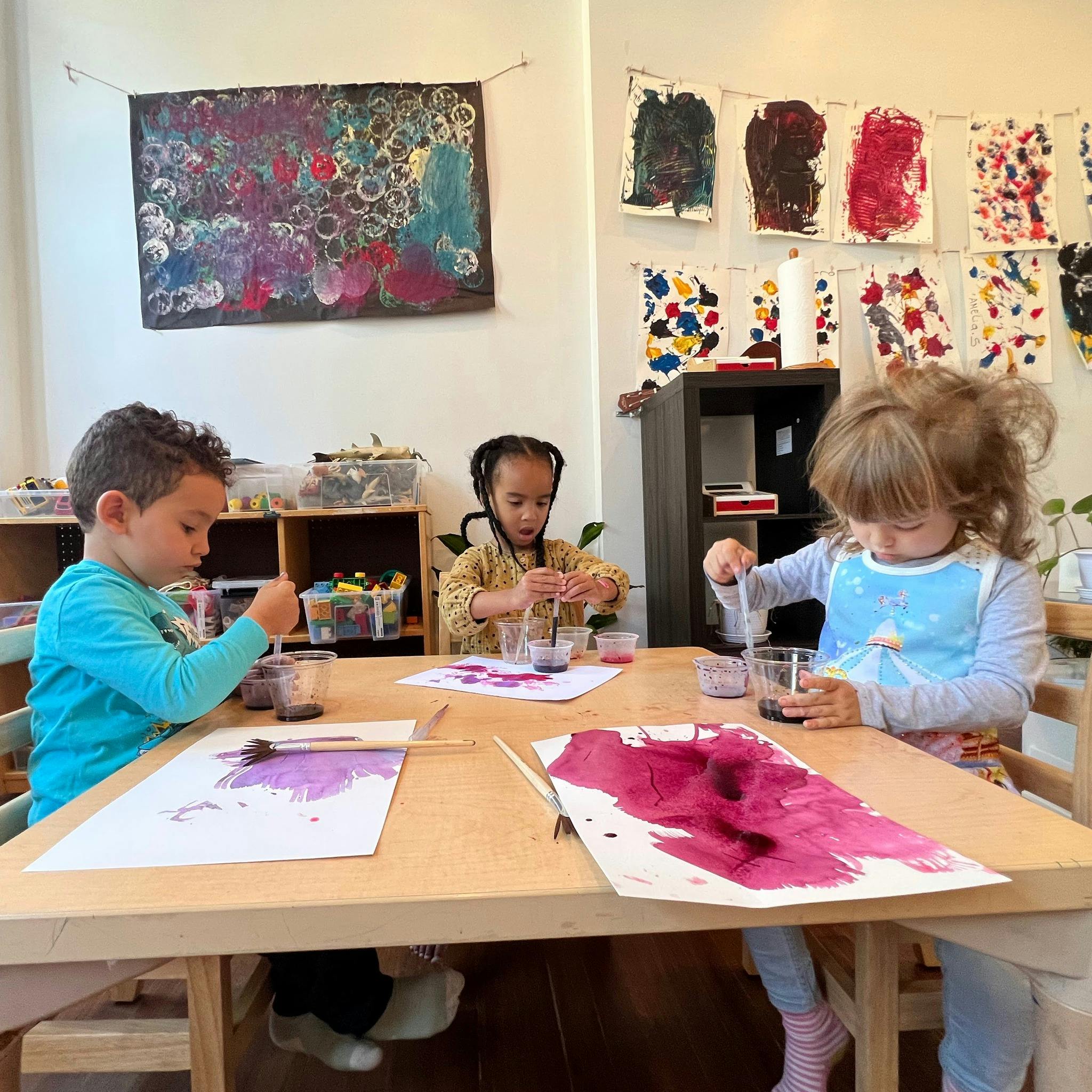 Three children painting at a table in a classroom