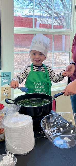 Child in chef hat and apron stirring a pot with a spoon