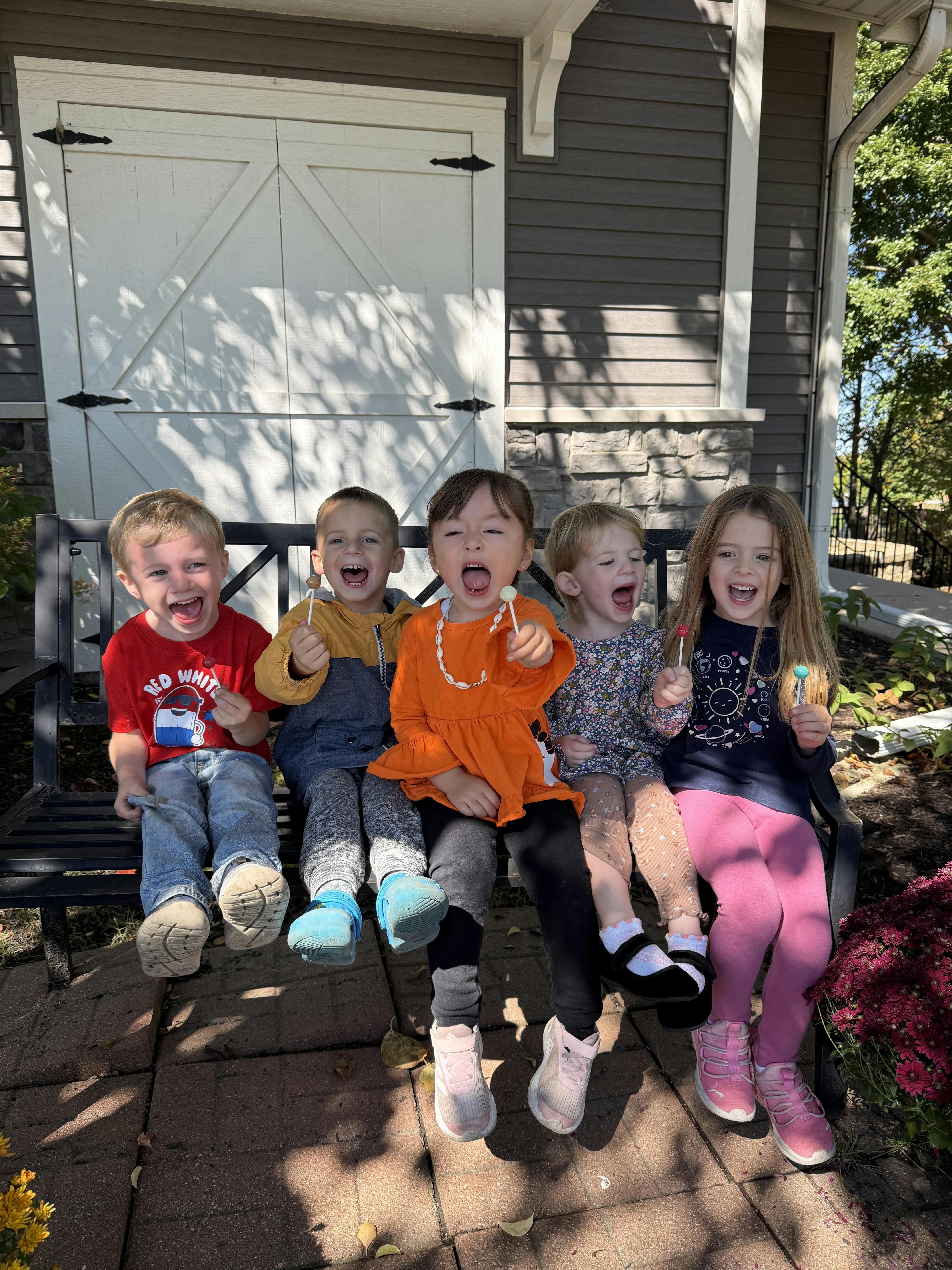 Five children sitting on a bench holding lollipops