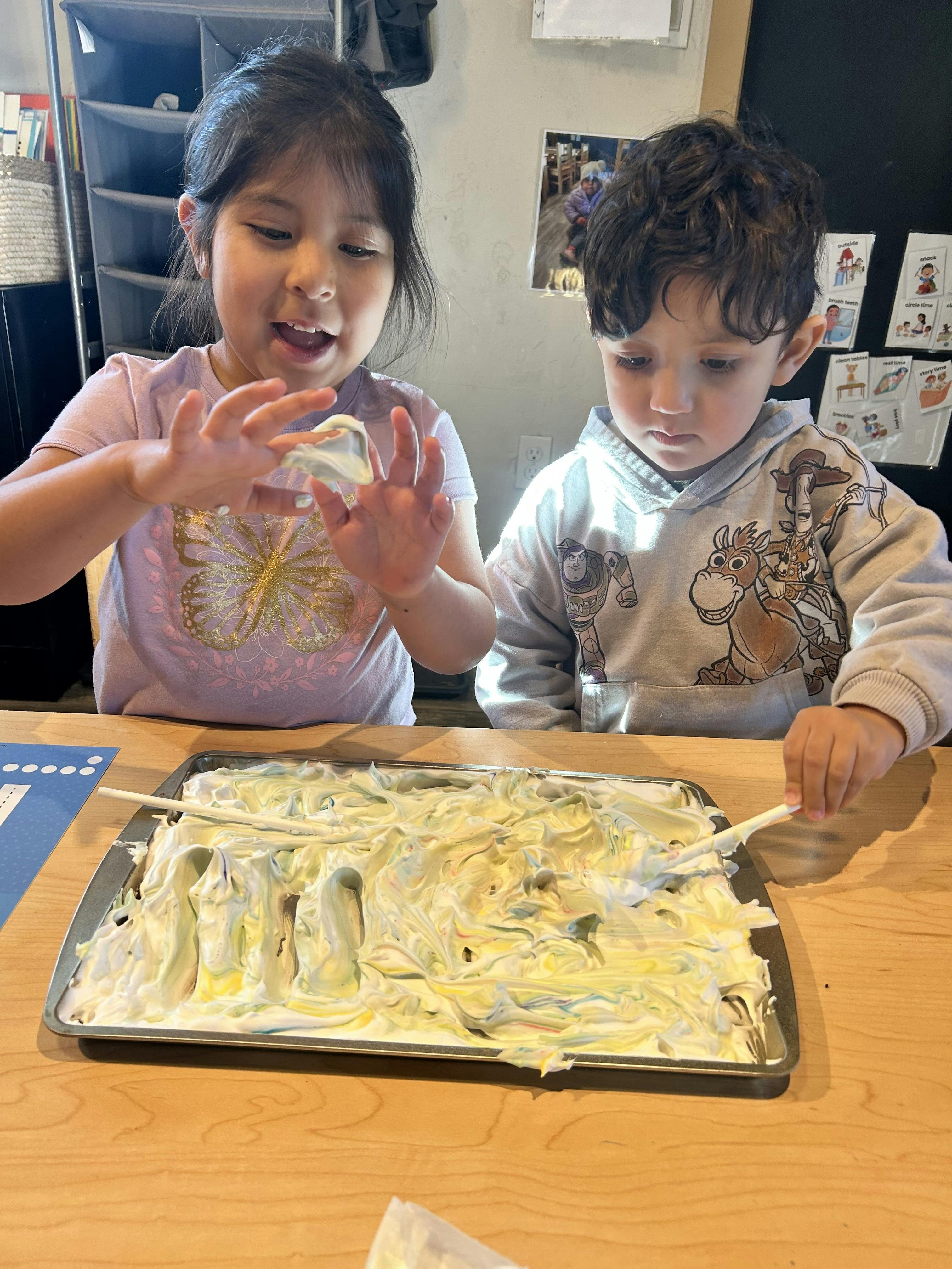 Two children playing with a tray of shaving cream