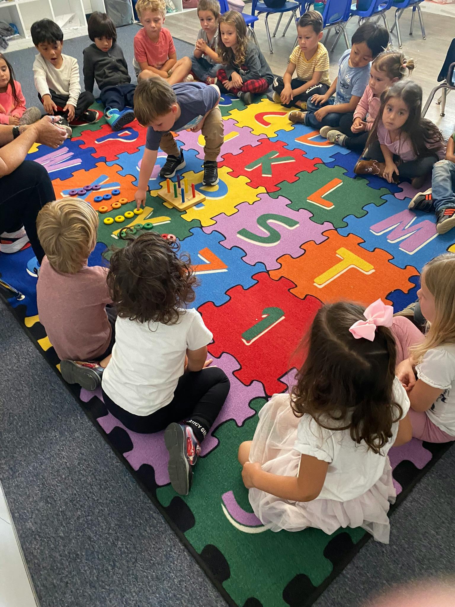 Children sitting on a colorful alphabet mat, one child playing with a toy