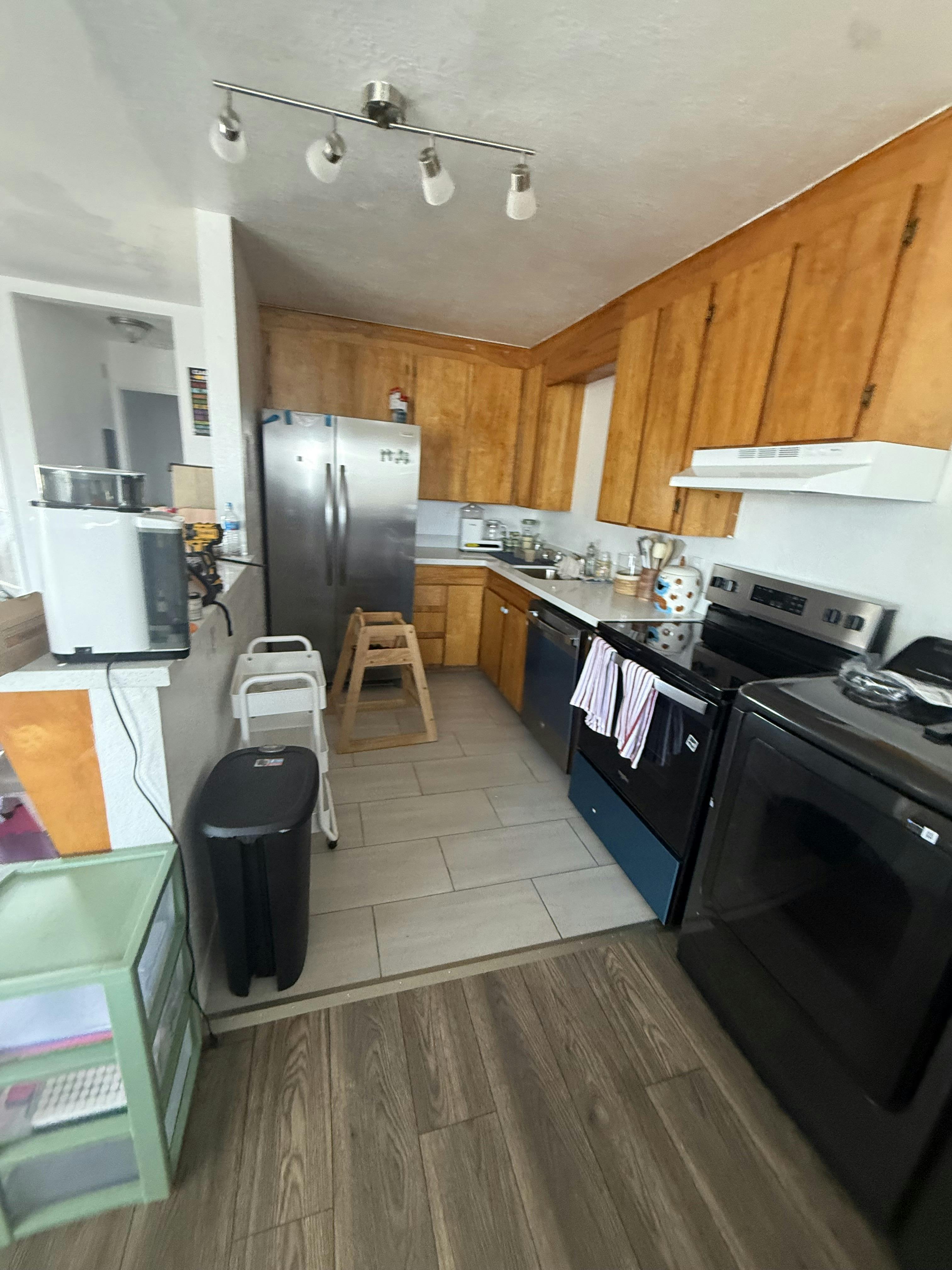 A full kitchen with light wood cabinets, stainless steel appliances, and a tiled floor