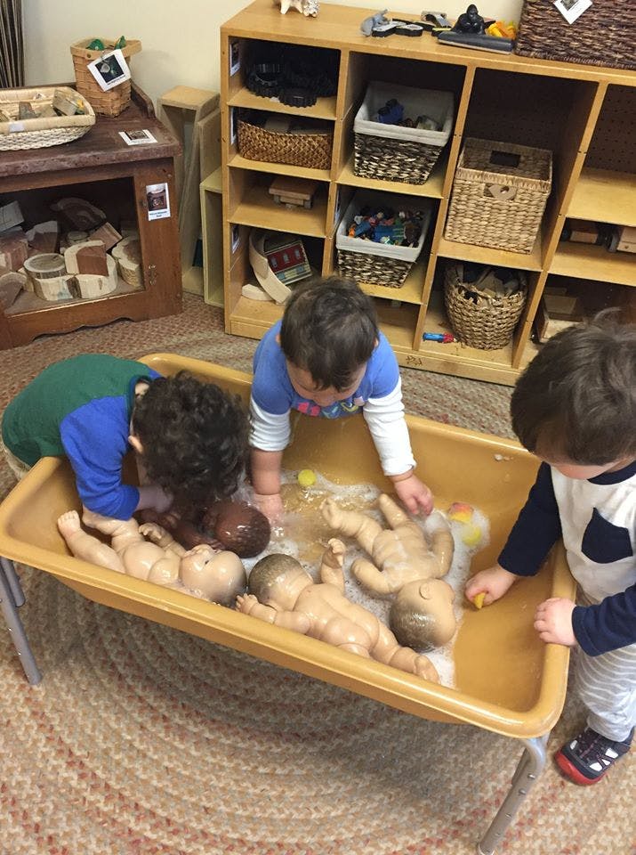 Three children playing with baby dolls in a tub of water