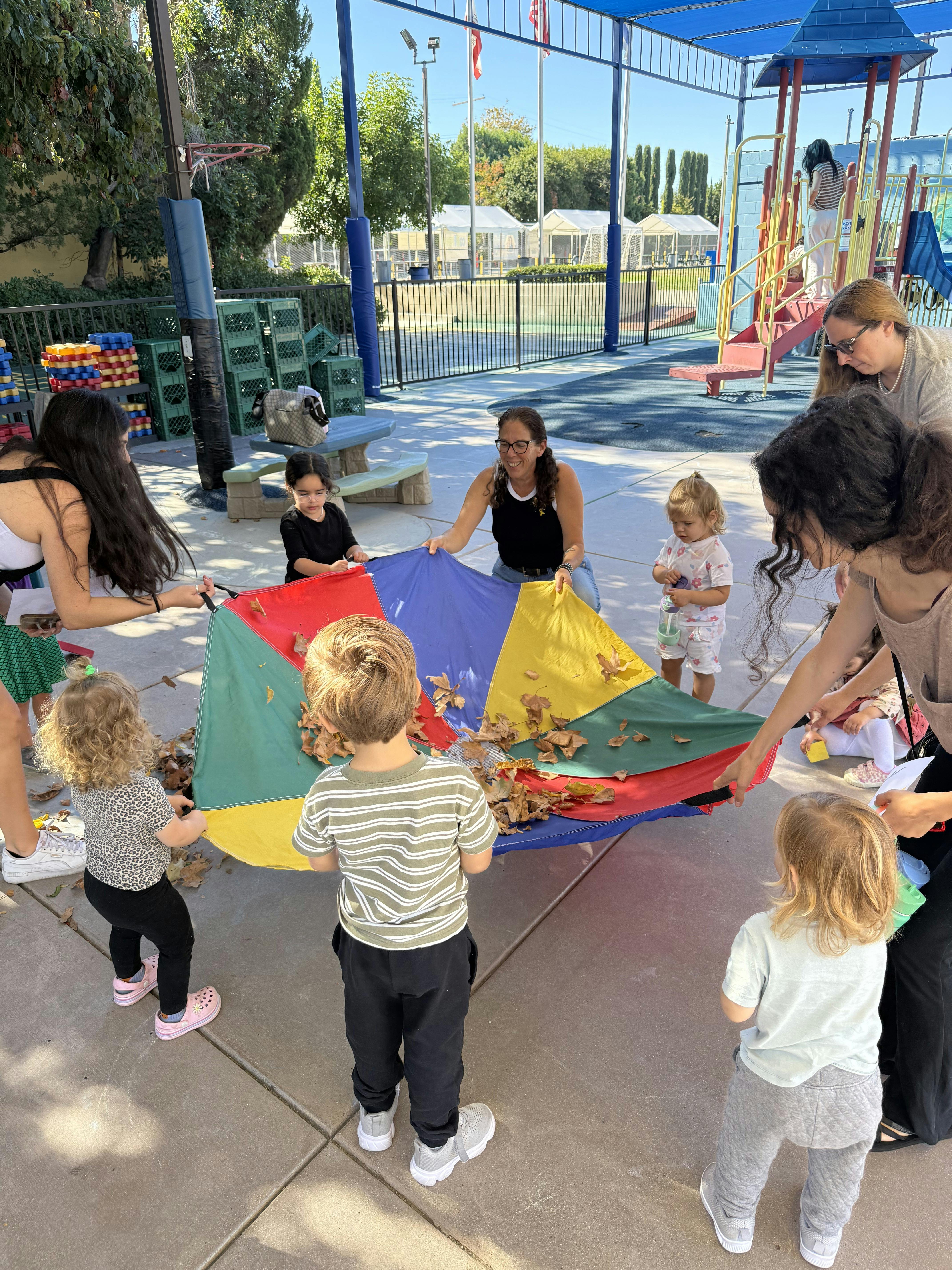 Adults and children holding a colorful parachute with autumn leaves on it