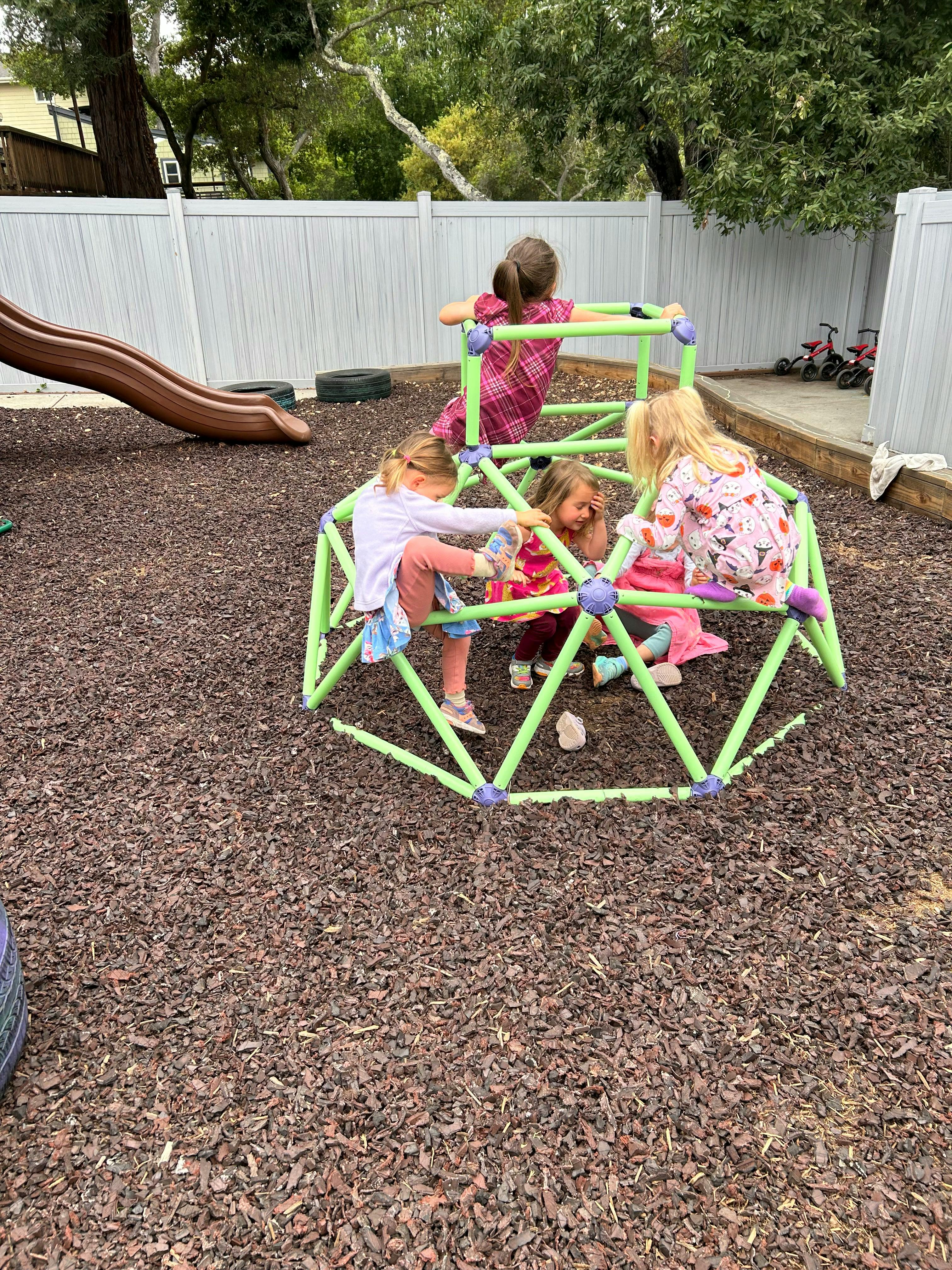 Children climbing on a green geodesic dome climber on a playground