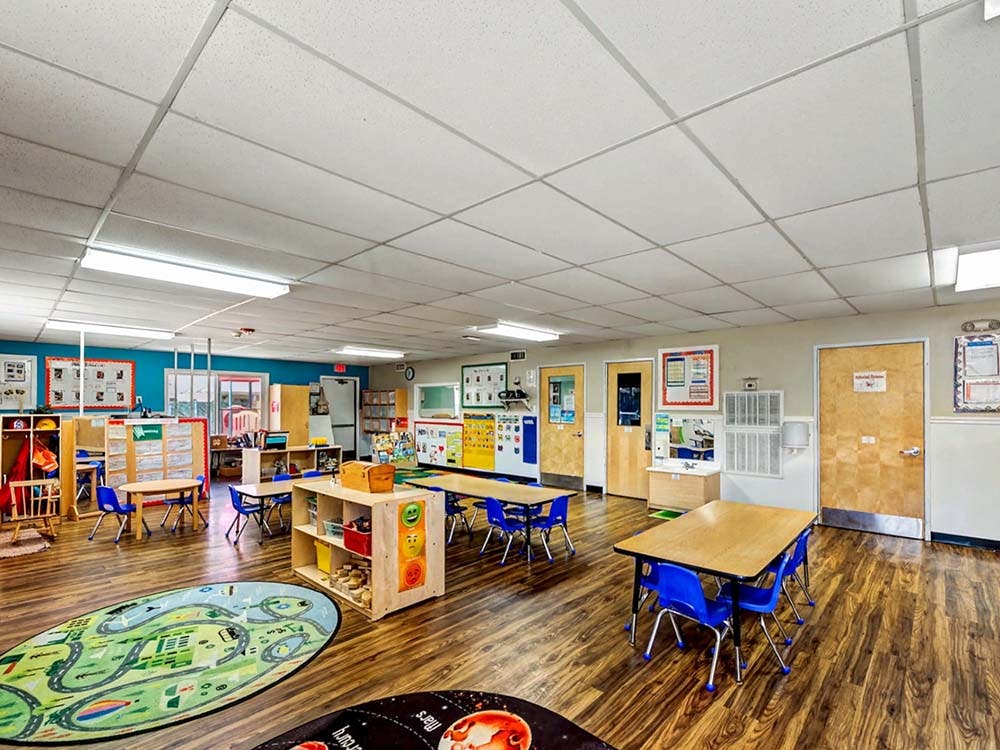 Empty classroom with small tables and chairs, play mats on the floor
