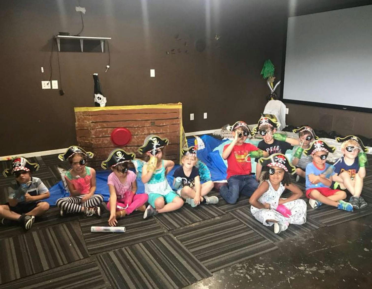 Children wearing pirate hats and eye patches sitting on the floor