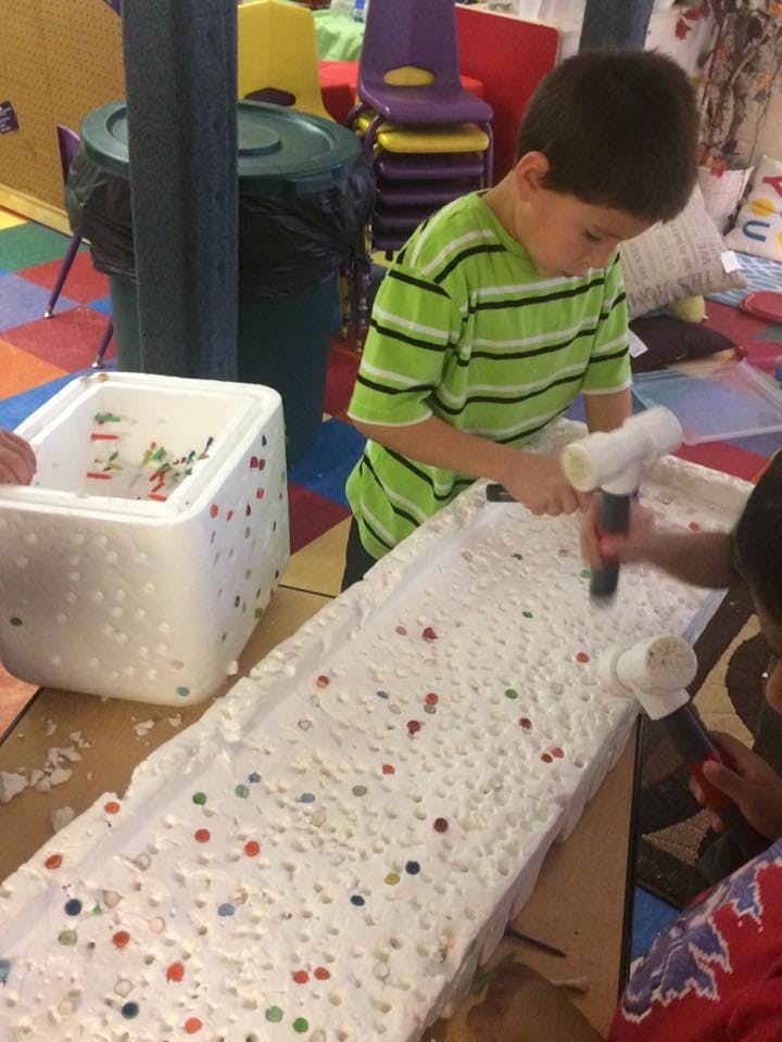 Child using a hammer to tap small objects into a white surface