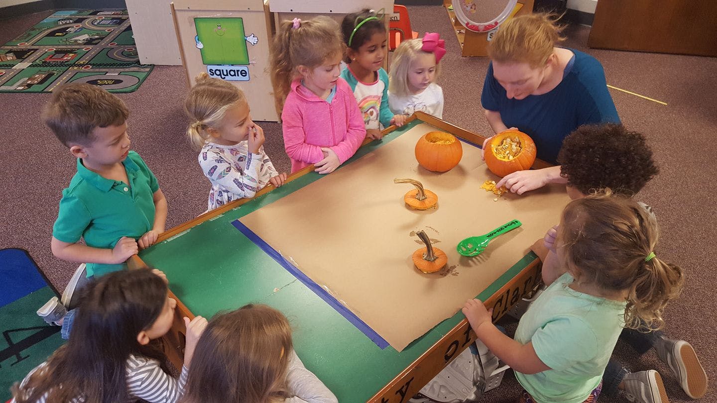 Adult and children gathered around a table with small pumpkins