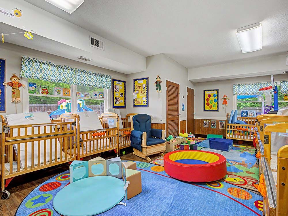 Cribs and play areas in a bright nursery room with windows overlooking a playground