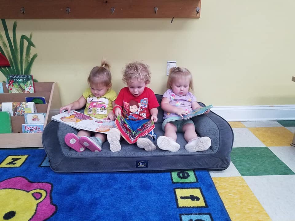 Three children sitting on a small couch reading books in a classroom