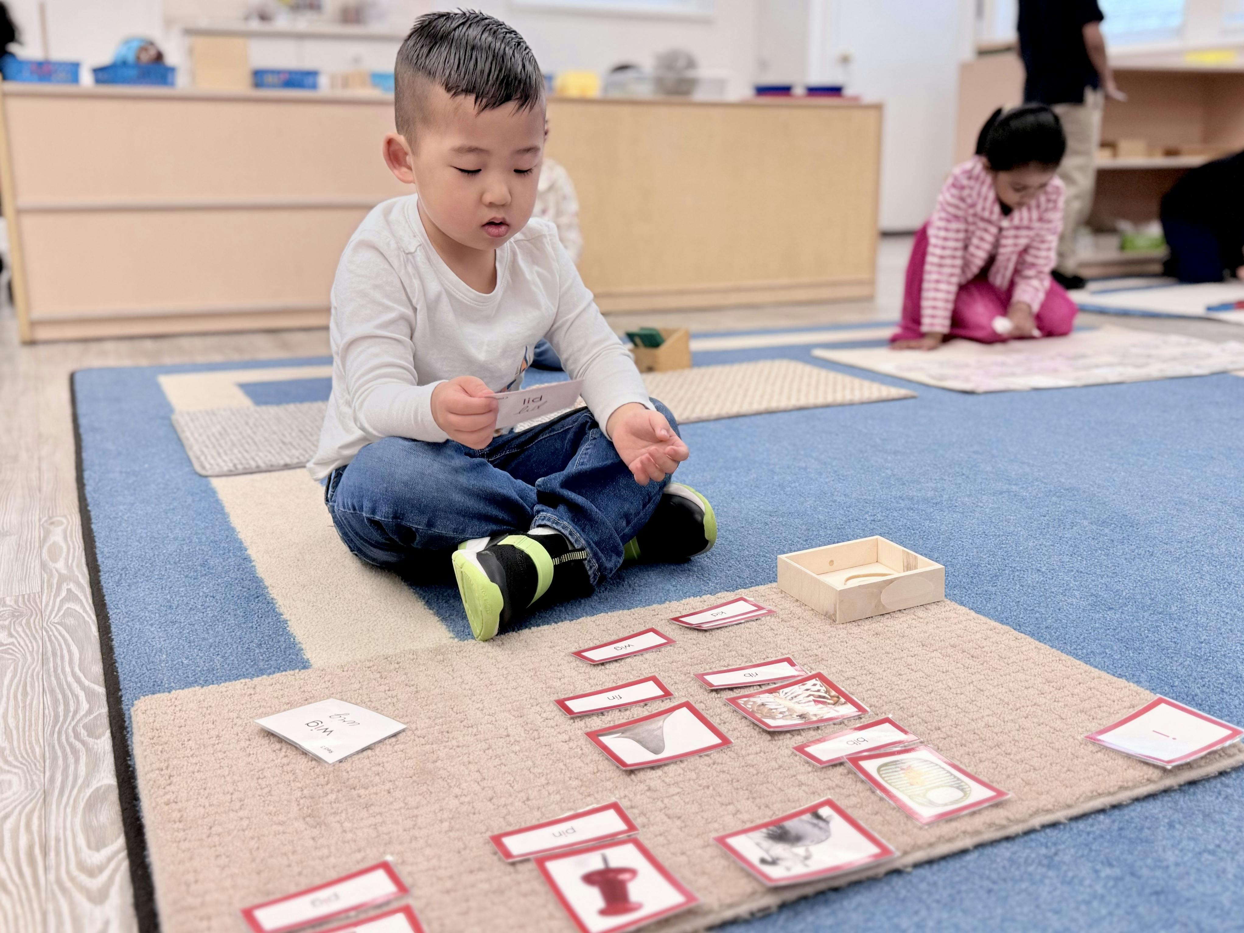 Child sitting on a rug, holding a learning card, with other cards spread around