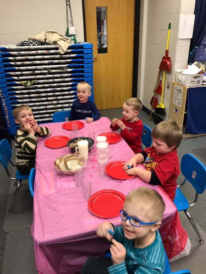 Children sitting around a table with red plates in a classroom
