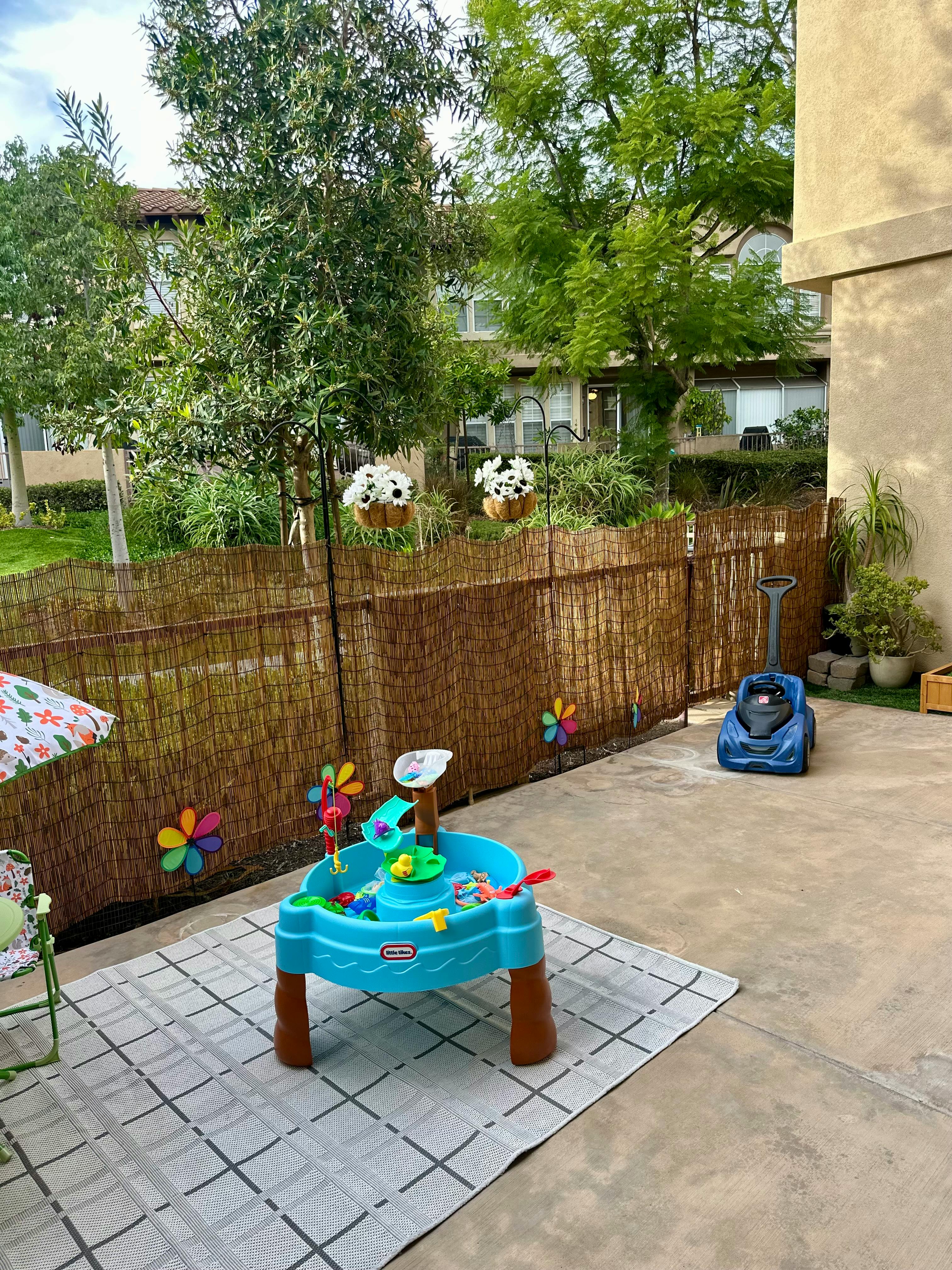 Outdoor patio with a blue water table on a rug next to a bamboo fence