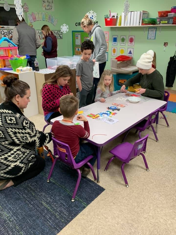 Adults and children gathered around tables in a classroom