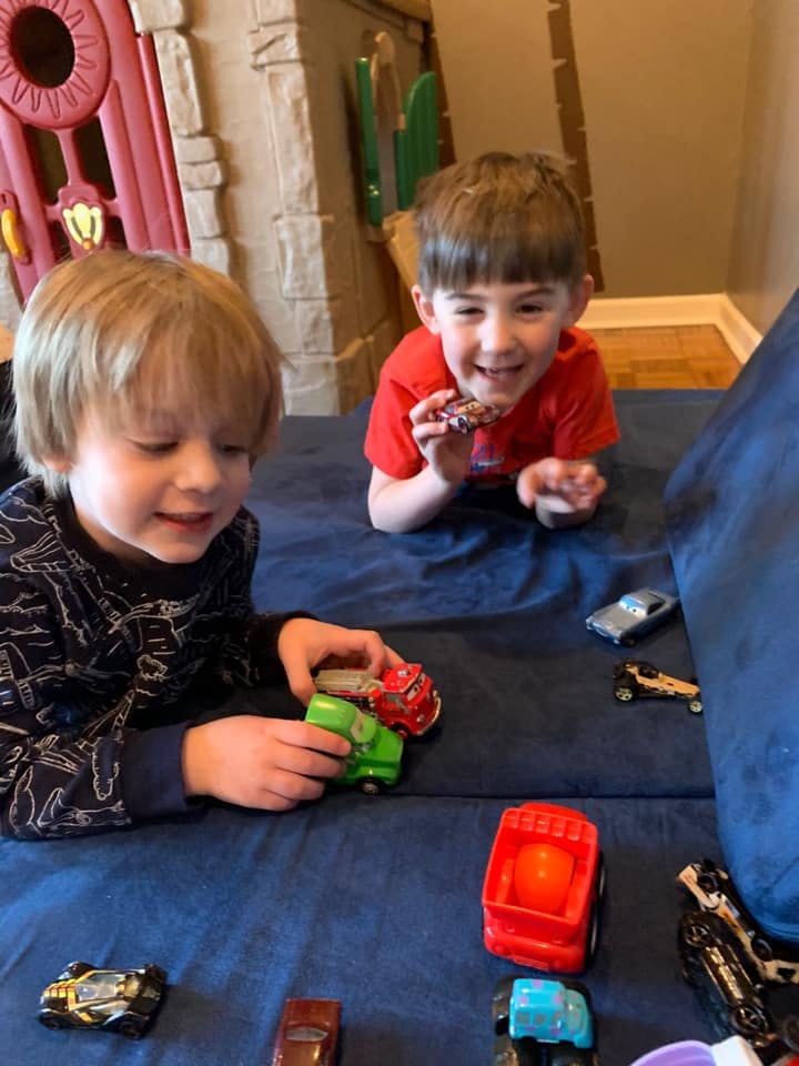Two children playing with toy cars on a blue surface