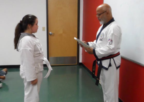 Adult and child in martial arts uniforms facing each other, adult holding papers