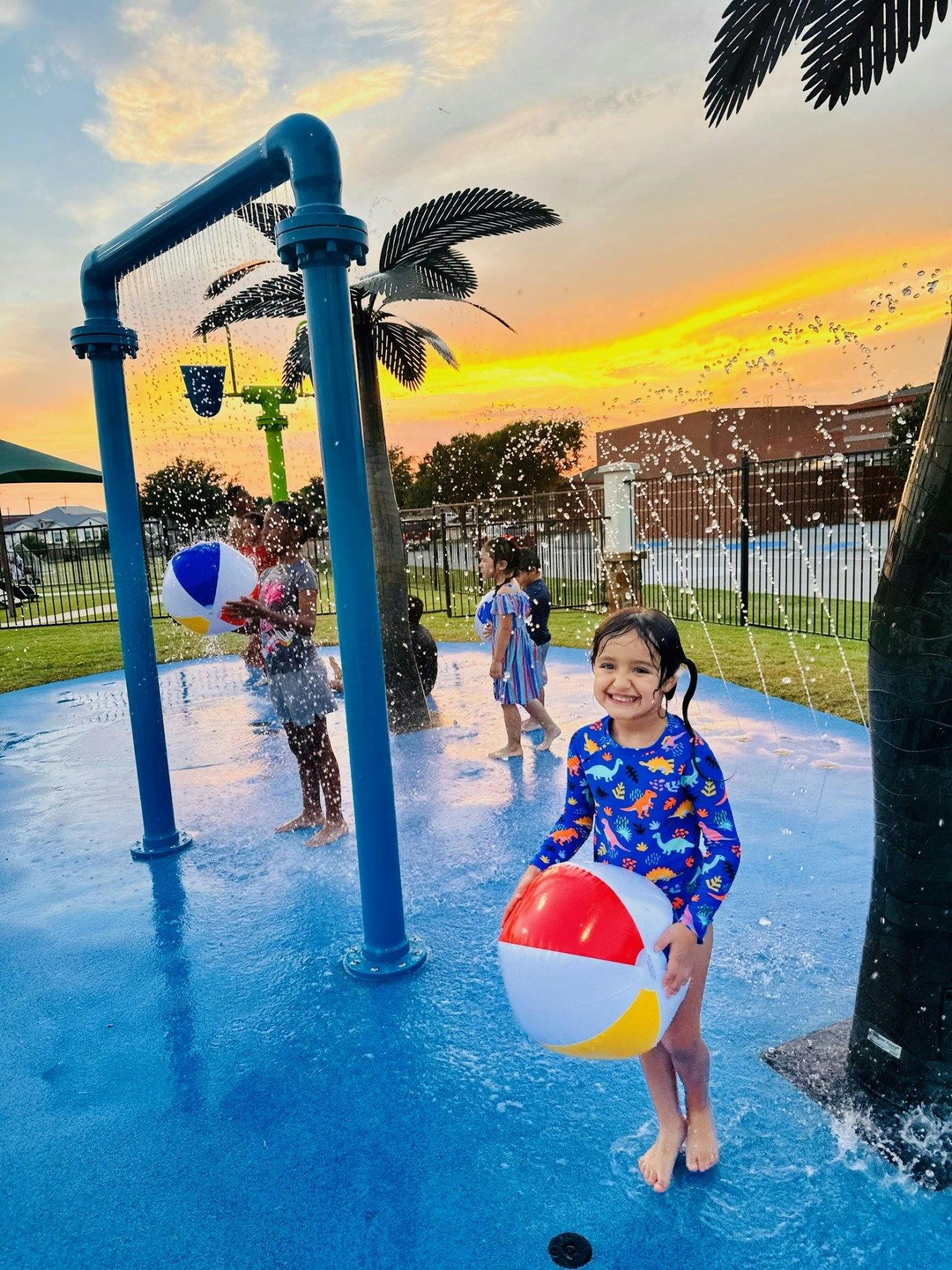 Children playing with beach balls at a splash pad during sunset