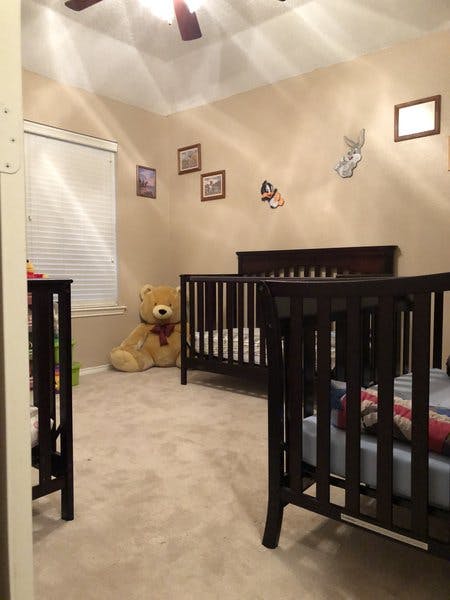 Two dark wood cribs in a child's bedroom with a large teddy bear