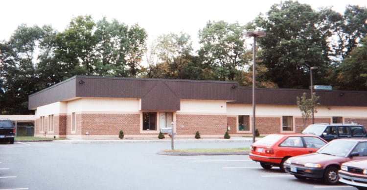 Building with a brown roof and brick facade, with cars in a parking lot