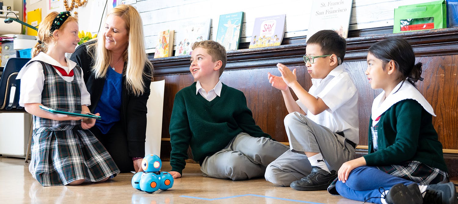 Teacher and three children sitting on floor with a robot, fourth child facing away