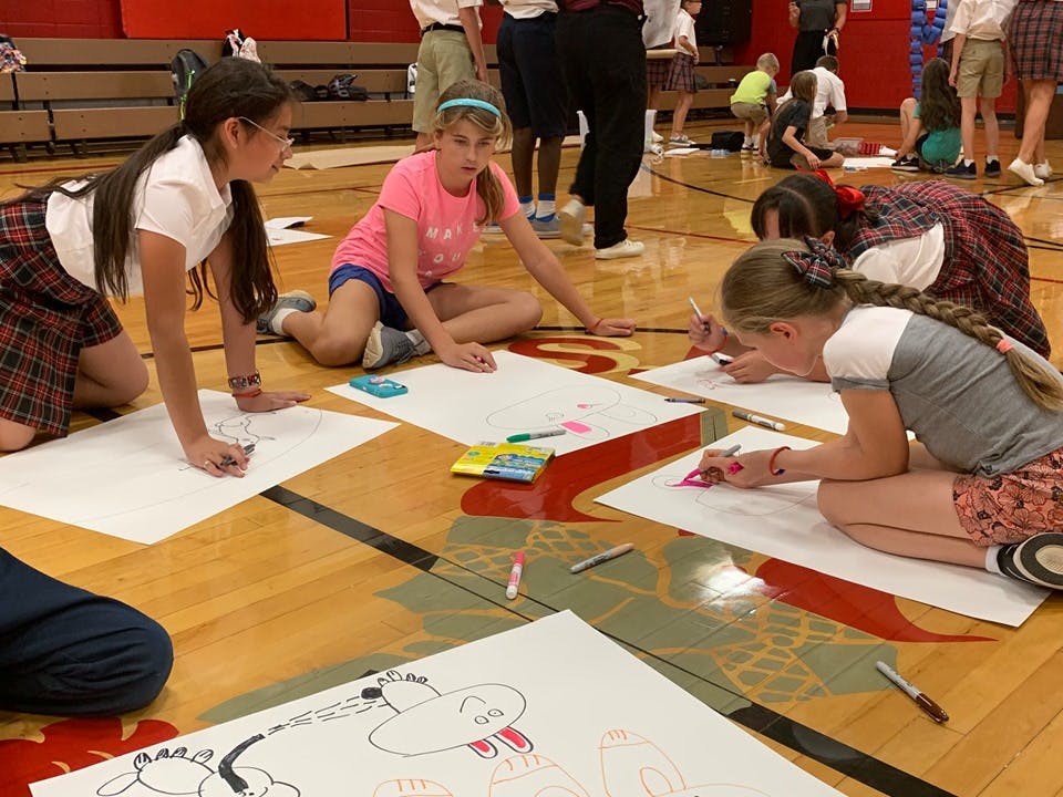 Children drawing on large sheets of paper on a gym floor