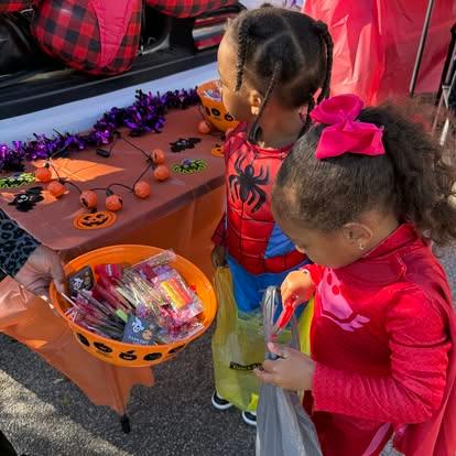 Two children in costumes picking candy from a bowl at a trunk or treat event
