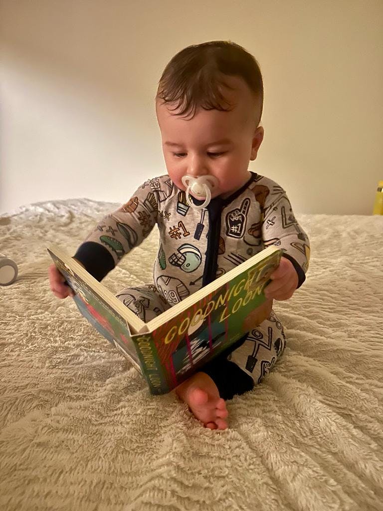 Child with pacifier reading a book titled "Goodnight Moon"