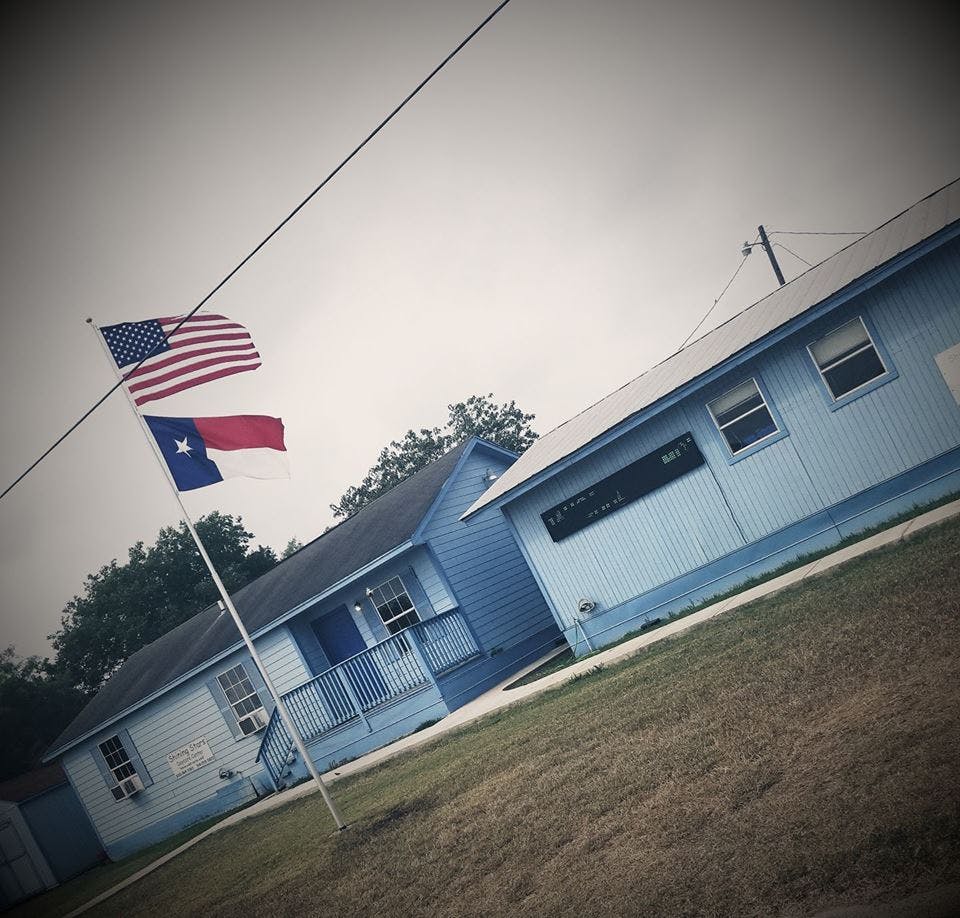 American and Texas flags flying on a pole in front of light blue buildings