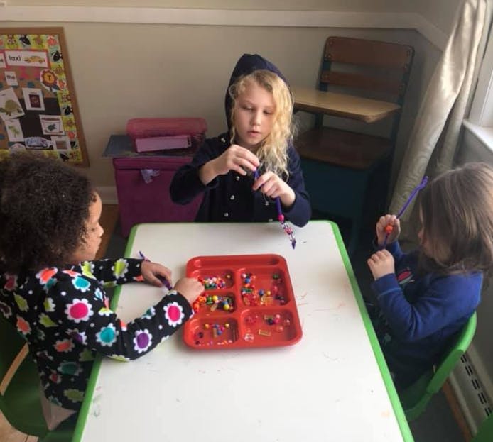 Three children making crafts with beads at a table