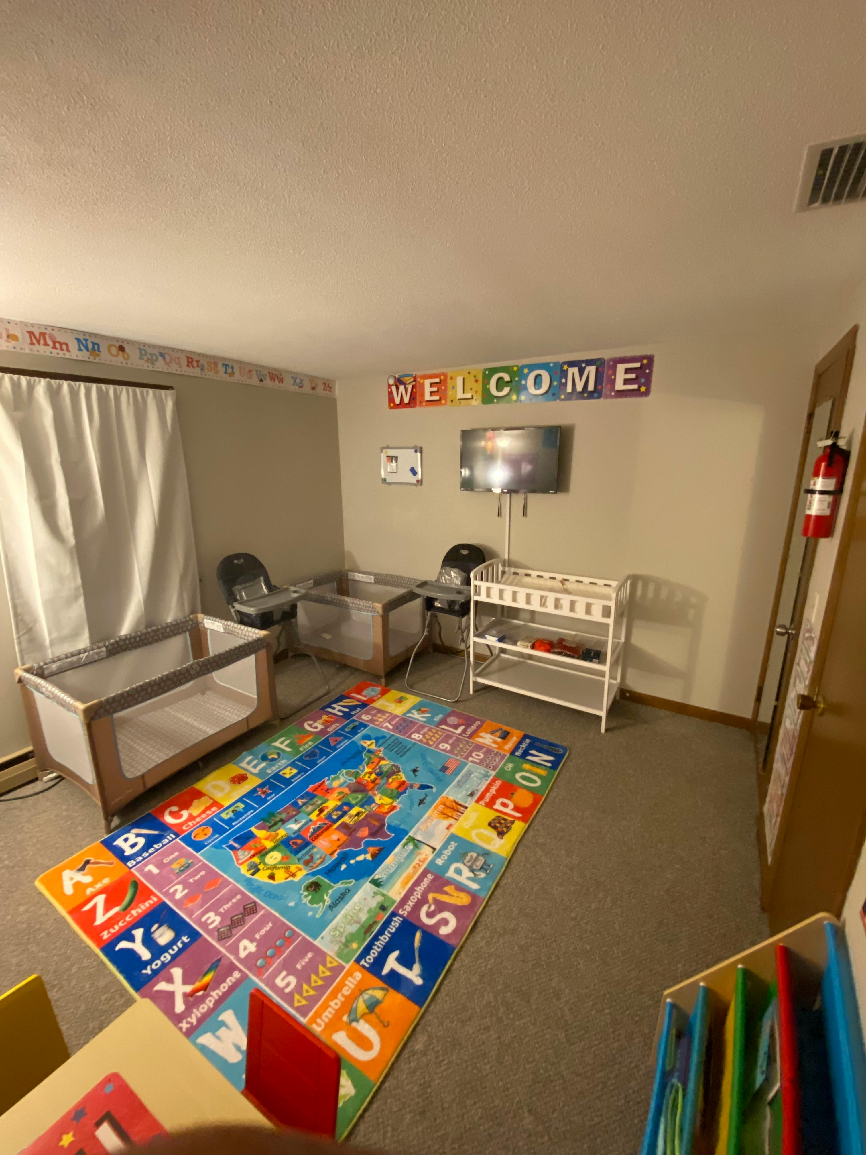 Room with two cribs, a changing table, and a colorful alphabet rug